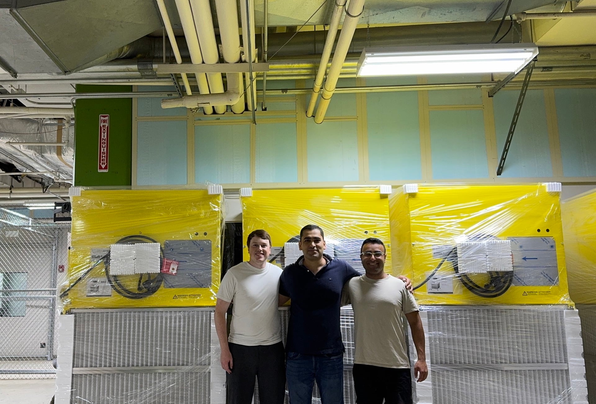 Three team members standing beside industrial air filtration units on the factory floor.